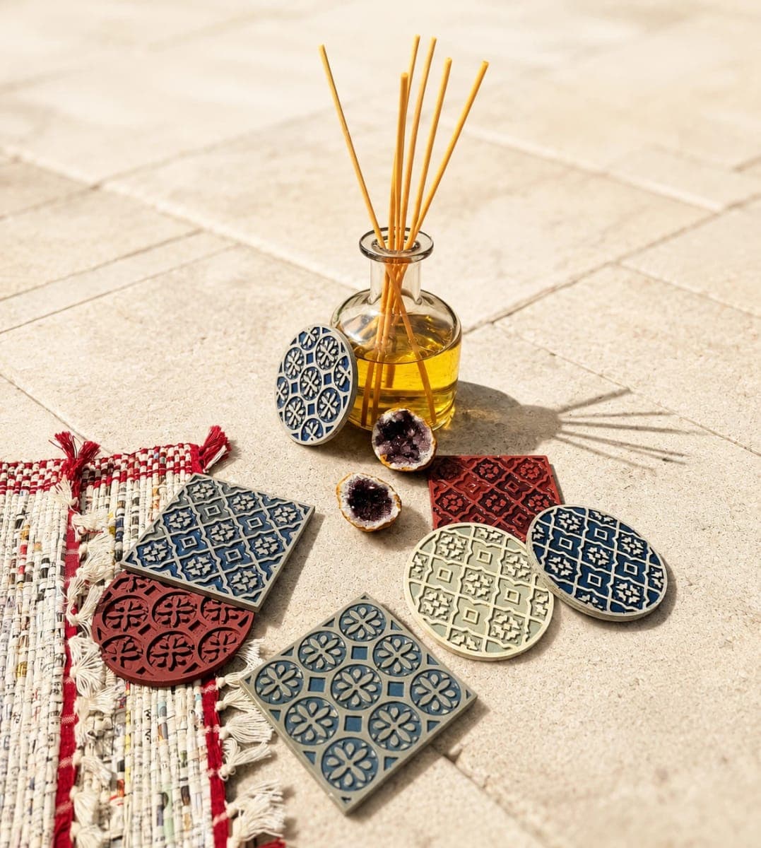 Cast coasters in blue, red and cream on stone tile, beside a reed diffuser, amethyst geodes and a hand-woven rug
