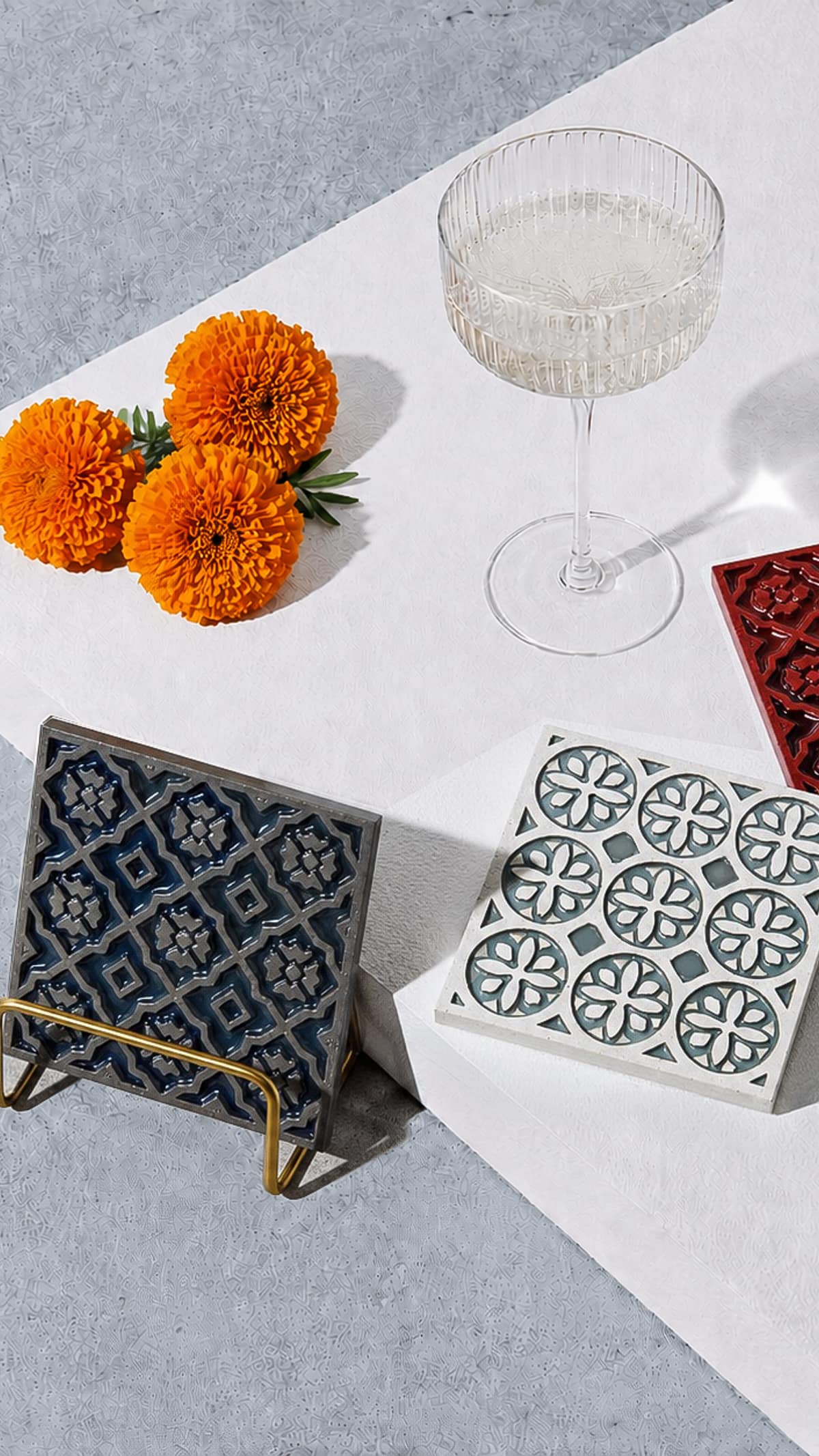 Cast concrete coasters arranged with marigolds and a coupe glass on a plaster surface